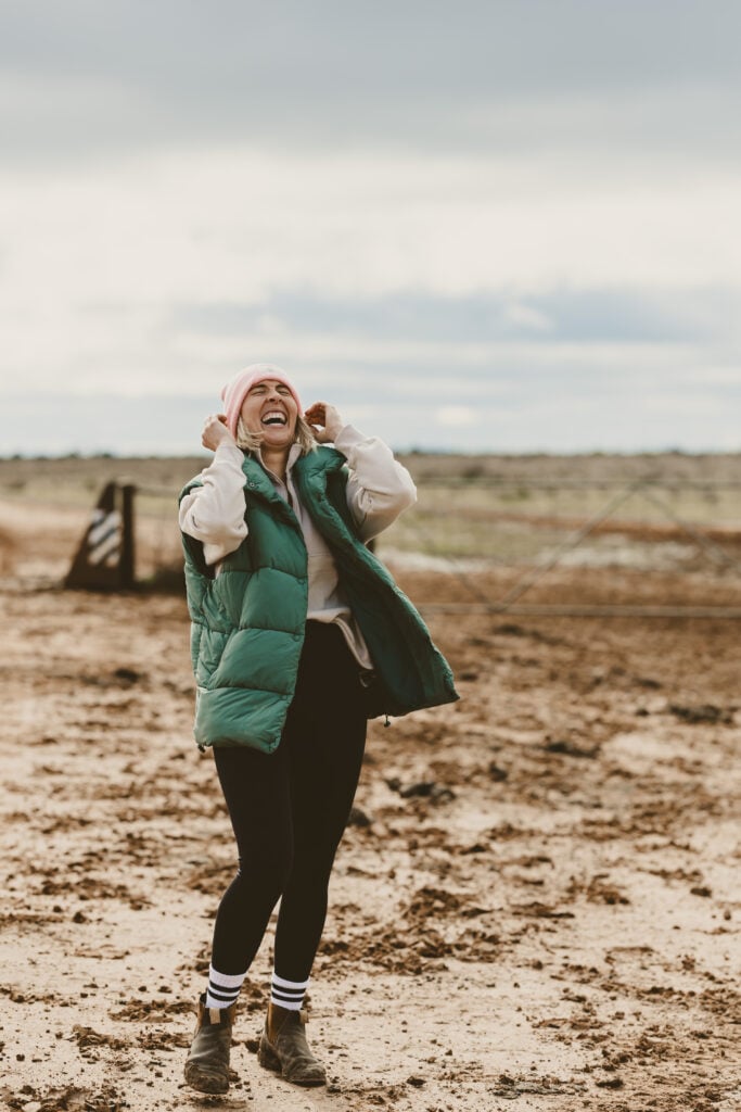 Laughing woman in beanie and green puffer vest outdoors