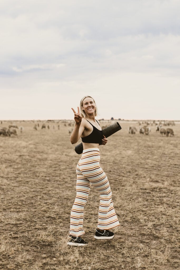 Smiling woman with yoga mat in a sheep field